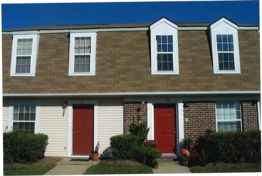 Two Kent Island Village townhome units with red doors, brick and shingle fronts, under a clear blue sky