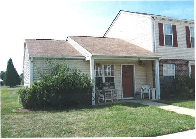 A Kent Island Village townhome end unit with a red door, a plant-filled front porch, and a green lawn