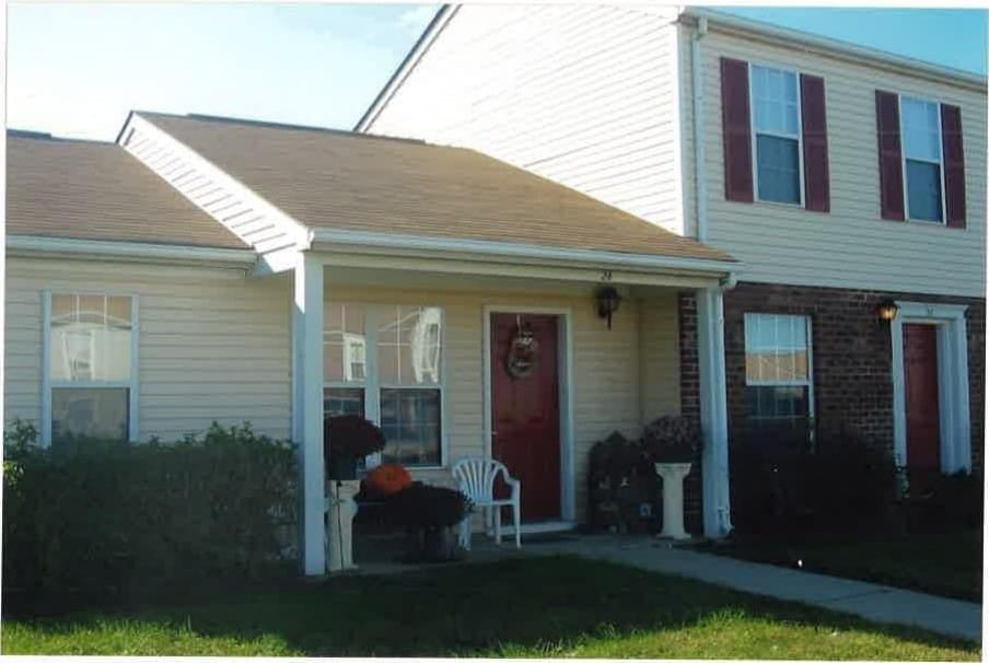 A Kent Island Village townhome with a covered porch, red door, and brick and light-sided fronts on a sunny day