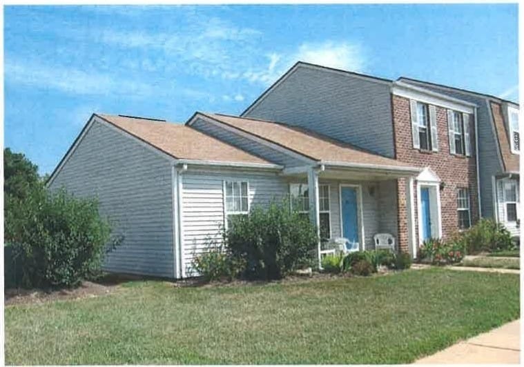 A Kent Island Village townhome building with gray siding, brick, blue doors, and a covered porch beside a green lawn