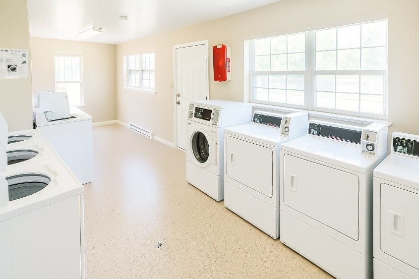 The community laundry room at Kent Island Village with several commercial front- and top-load washers and dryers, utility sinks, and large windows