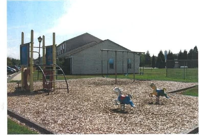 Swings and spring-riders on the wood-chip playground at Kent Island Village, with a townhome building behind